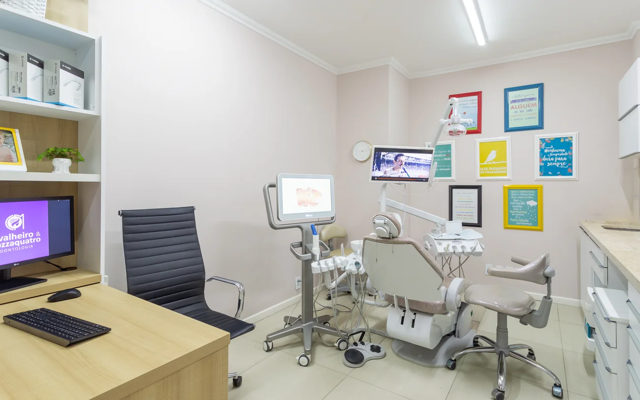 Consultório da clínica com cadeira odontológica, equipamentos e iluminação natural.