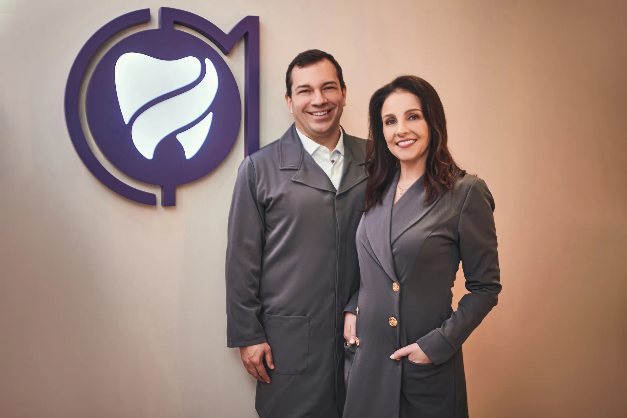Charles Cavalheiro e Lisandra Mozzaquatro na clínica, com a marca ao fundo.